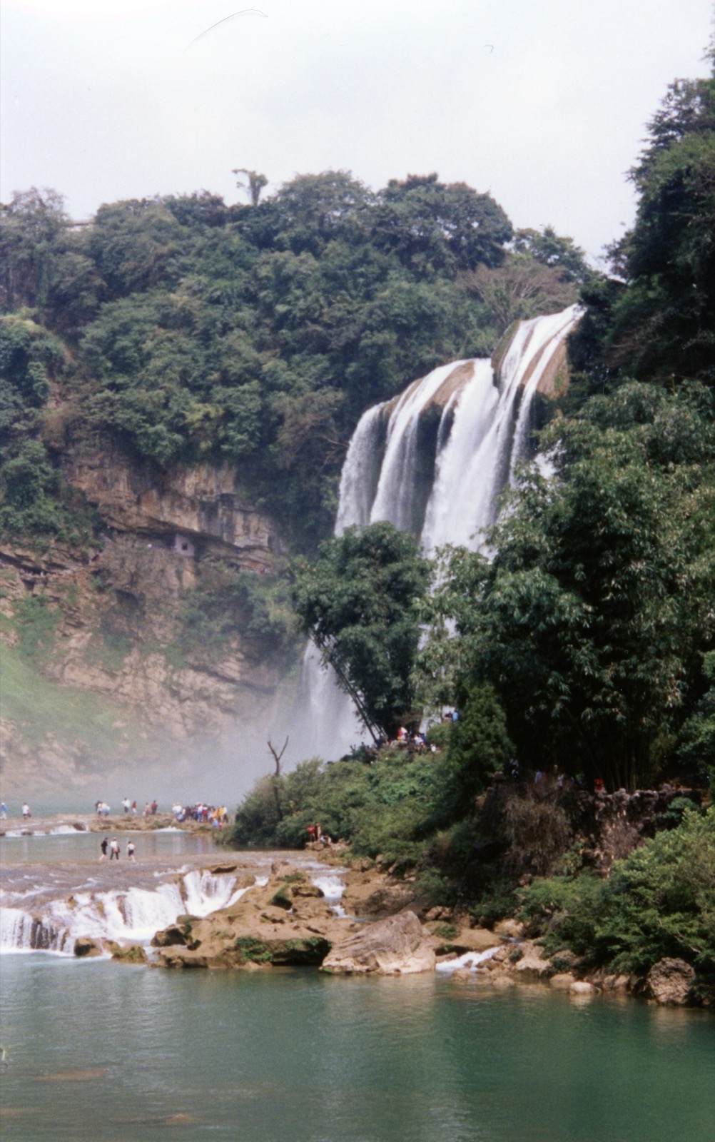 Huangguoshu Waterfall in Guizhou surrounded by green cliffs and water.